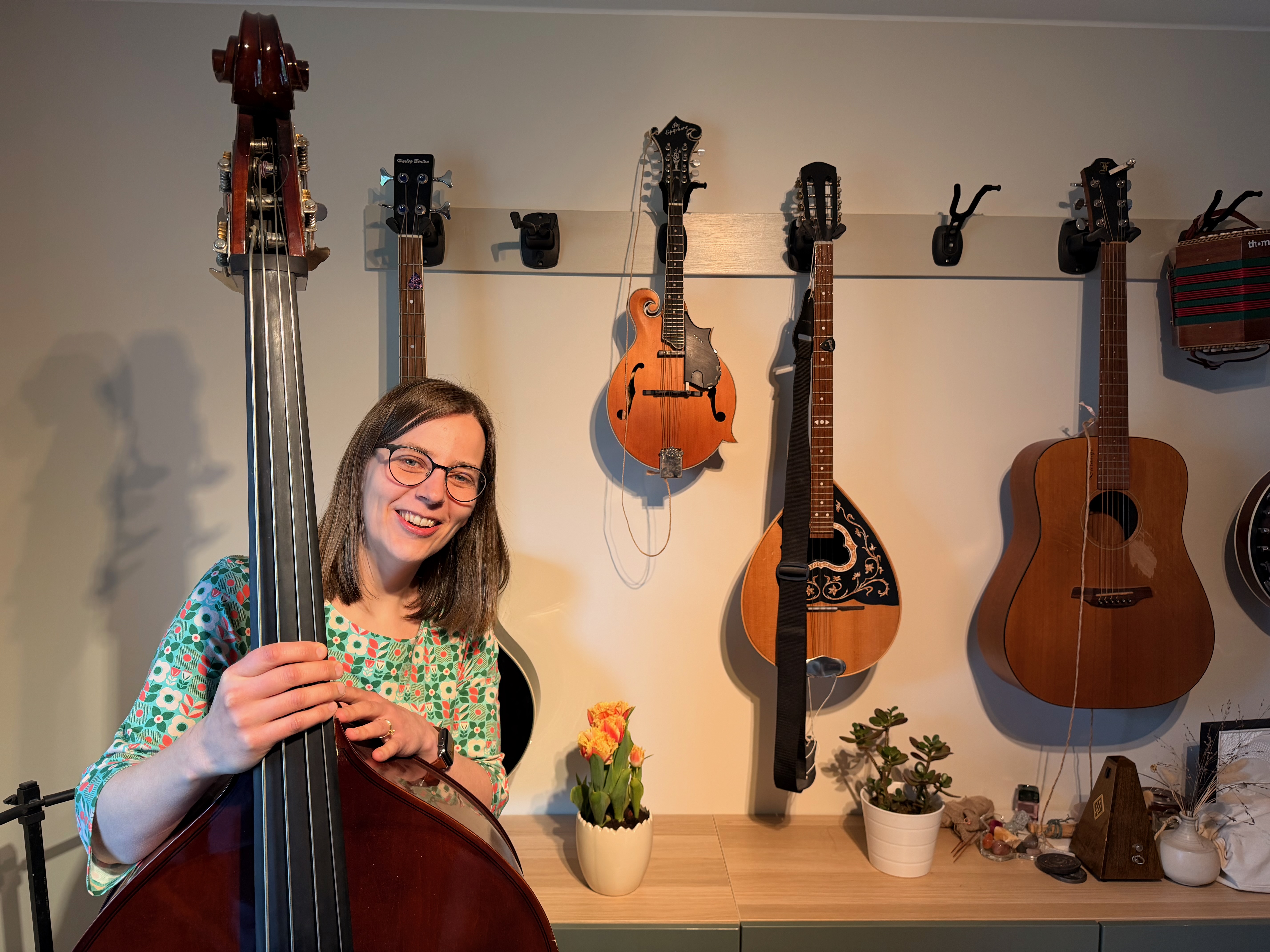 Julia Ljungström-Caunt håller sin kontrabas framför en vägg med mandoliner, gitarr och dragspel.